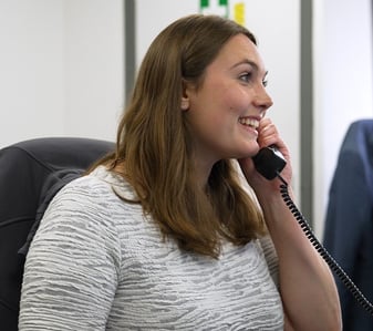 Friendly female office employee talking on the phone at her desk, smiling while assisting a customer.